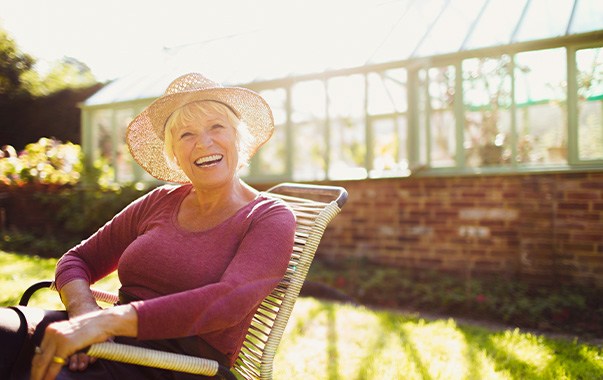 Woman in garden chair outside with straw hat smiling in sunshine