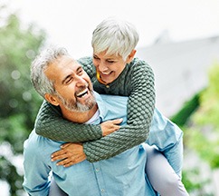 Woman in green sweater piggy-back-riding a man in a blue shirt outside laughing