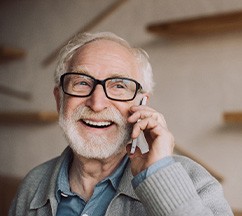 Man with white hair, black glasses, and a grey sweater talking on his smartphone