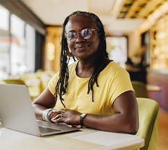 Woman in a yellow shirt sitting at a table with laptop 